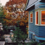 A twilight view down a concrete and masonry walkway, wooden privacy fence on one side, blue craftsman house on the other with windows illuminated.