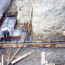 An angle from above of a man working on forms for concrete footings at the bottom of an excavated hillside.